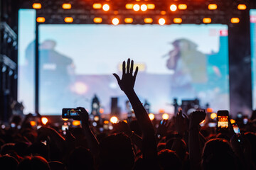 Crowd cheering and filming with smartphones at concert with big screen