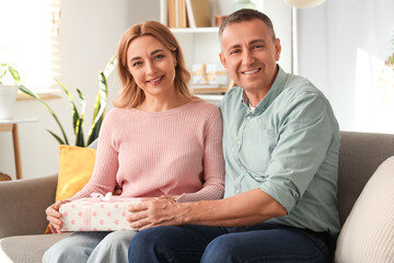 Middle-aged couple with gift box sitting on sofa at home. International Women's Day