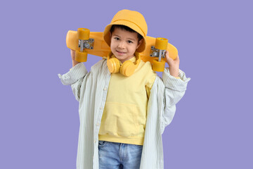Cute little Asian boy in adult clothes with skateboard on lilac background