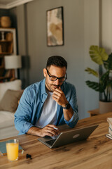 Obraz premium Man seated at a table reviewing expenses while typing on his laptop