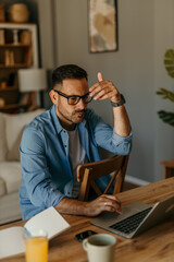 Obraz premium Professional man multitasking with a laptop and documents in a contemporary home setting