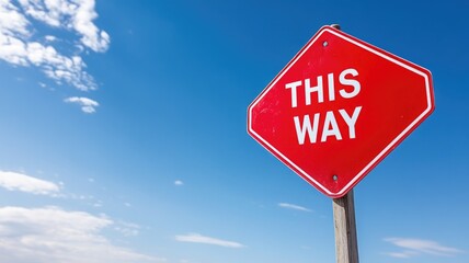 Red direction sign with "THIS WAY" text against clear blue sky
