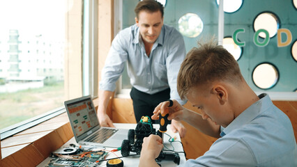 Caucasian teacher help student fixing car model and giving advise for programing system or coding...