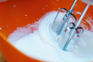 metal mixer whisks beating a translucent egg white into a stiff white foam, set against a vibrant...