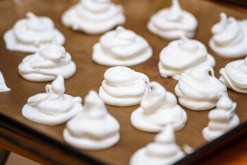 Delicate meringue peaks rest on a baking tray, ready for baking. These fluffy white confections...