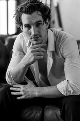 Portrait of a handsome young sexy man in a white shirt, jeans jacket posing in studio with a loft interior. Black and white. Casual clothes, modern style