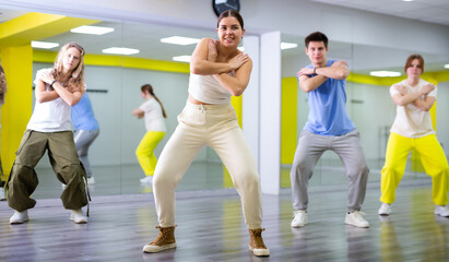 Class of young fit teenagers in casual wear dancing together during training in spacious studio