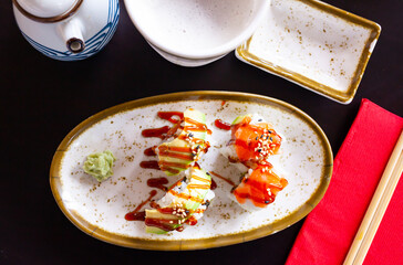 Traditional Japanese food appetizer - uramakizushi rolls with filling of raw salmon and avocado seasoned with unagi sauce and sesame seeds, served with with spicy wasabi and soy sauce