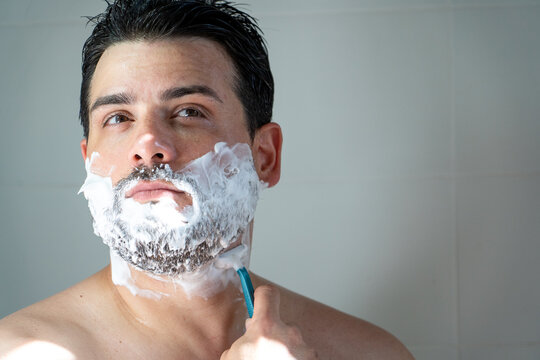 Hombre apuesto afeit&aacute;ndose la barba, usando espuma y m&aacute;quina de afeitar