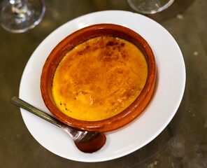 Delicious traditional Spanish dessert - Crema catalana served with spoon in clay bowl in restaurant