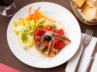 On white background there is plate with beautifully laid baked eggplant, onion, red bell pepper. Traditional escalibada with anchovies and fresh vegetable salad.