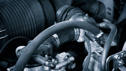 A close up of a car engine with a hose wrapped around it. The hose is black and the engine is black
