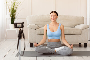 Online Meditation. Yoga Blogger Woman Making Fitness Blog Sitting In Lotus Position On Mat At Home. Selective Focus