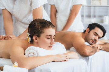 Caucasian couple customer enjoying relaxing anti-stress spa massage and pampering with beauty skin recreation leisure in day light ambient salon spa at luxury resort or hotel. Quiescent
