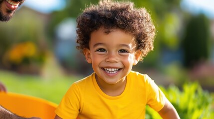 Little boy enjoys sunny day in wheelbarrow with dad in the garden