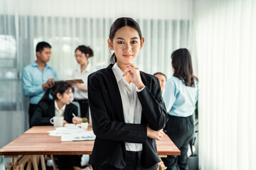 Portrait of happy young asian businesswoman looking at camera with motion blur background of business people movement in dynamic business meeting. Habiliment