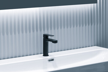 A black faucet is mounted on a white sink. The sink is clean and shiny, and the faucet is the only visible object in the image