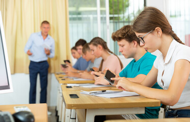 Teenager students sitting in class room and using their smartphones.