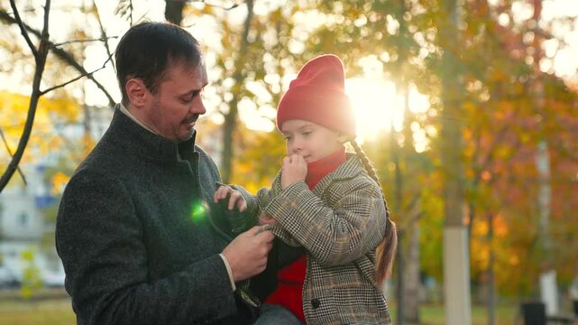 Dad listens attentively to emotional daughter talking about impressions of walk. Dad adjusts hat on head of daughter with care. Positive daughter sits with dad in park sharing plans for next stroll