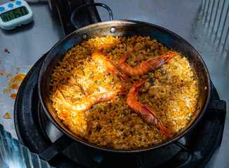 Sea paella is cooked on camping gas stove. Process of cooking seafood paella in large frying pan. Dish is supplemented with several tiger shrimps