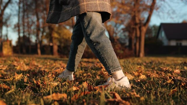 Child relishes delightful sound of rustling leaves walking along grassy path at sunset. Child enjoys sensation of walking on crunchy leaves. Child enjoys simple pleasure of walking on sunny day
