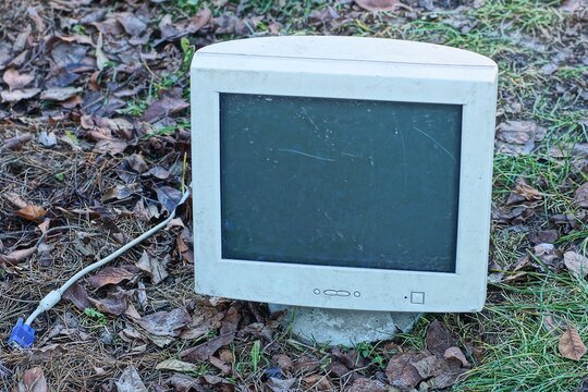 one dirty old discarded plastic gray with glass screen retro broken electronic with cable computer monitor stands on the ground during the day outdoors