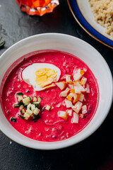 Vibrant beetroot soup with boiled egg, smoked chicken, and cucumber in a white bowl