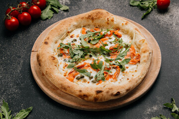 Gourmet pizza with smoked salmon, arugula, capers, and melted cheese on a wooden plate