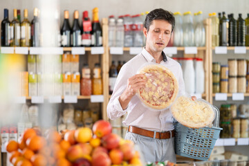 Man in light shirt took some varieties of frozen pizza from shelf. Client compare pizza with...