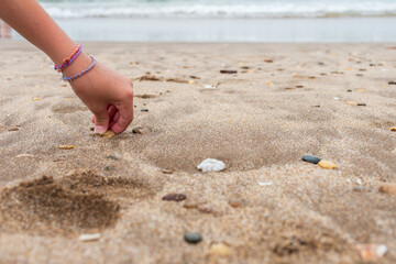 Child's hand picking up shells from the beach with copy space.