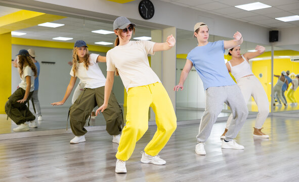 Diligent teenagers leaning back on their toes during modern dance rehearsal in spacious hall
