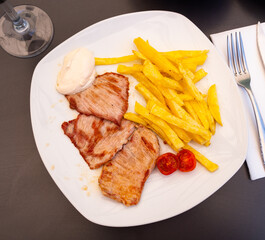 Hearty dinner from chef is on plate.Slices of fried pork tenderloin with French fries,garnished with cherry tomatoes and white hot sauce
