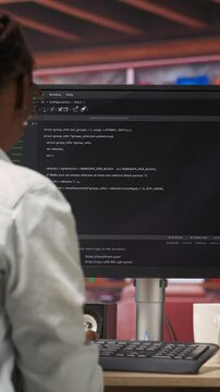 Vertical video Programmer types code into PC, entering commands, running script. African american IT professional in apartment fixing errors in application, implementing new features, camera B