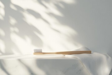 Bamboo toothbrush rests on a white marble surface with a soft towel, bathed in sunlight.