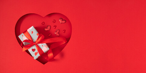 Festive red Valentine's Day banner with gift and empty space. Beautiful gift with satin ribbon and...