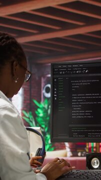 Vertical video Programmer types code into PC, entering commands, running script. African american IT professional in apartment fixing errors in application, implementing new features, camera A