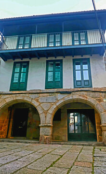 Fachada de casa antigua con ventanas de madera azul y arcos de pidra formando galerias.