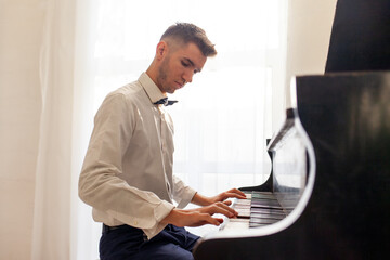 young guy in white shirt plays on old black piano, musician pianist performs melody on acoustic...