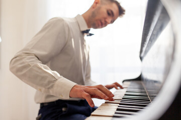 young guy in white shirt plays on old black piano, musician pianist performs melody on acoustic...