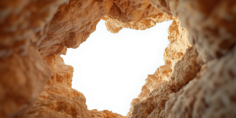 A unique perspective looking up through a natural rock formation with rugged, textured walls. The earthy tones of the rocks contrast against the bright white sky