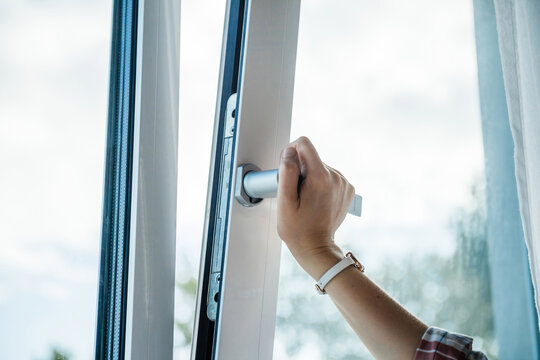 A professional close-up of a woman right hand turning the handle to tilt a luxury PVC window, highlighting superior craftsmanship, durability, and modern functionality.