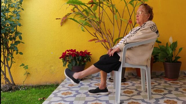 Senior woman exercising legs and ankles with circular movements in coordinated manner, sitting on chair in garden. Concept of home exercise for seniors and healthy lifestyle