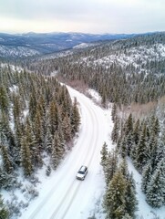 Aerial view of a car driving on the highway road in a snowy forest, during winter time.