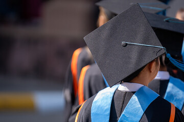 A group of people wearing graduation caps and gowns. The person in the middle is wearing a black cap with a blue ribbon