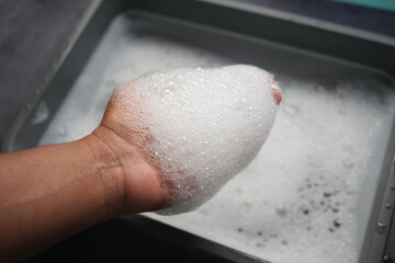 A Hand Holding Soapy Bubbles High Above a Washing Basin in the Kitchen