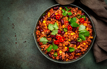 Chili con carne with minced beef, beans, paprika, corn, cilantro, jalapeno pepper in tomato sauce, tex-mex cuisine in green frying pan, top view