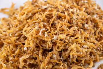 Crispy Golden Fried Anchovies on White Plate. A tantalizing close-up of crispy golden fried anchovies piled high on a pristine white plate against a minimalist white backdrop.