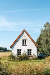 Obraz premium Charming white cottage with a red roof surrounded by green fields under a clear blue sky, located in a serene countryside setting
