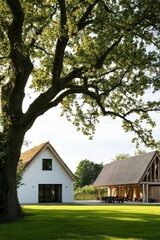 Nestled in a picturesque rural landscape, a contemporary country house stands alongside a traditional barn, both surrounded by a sprawling green lawn beneath the shade of a majestic tree on a bright.
