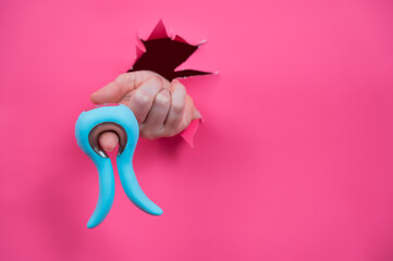 Female hand sticking out of pink paper background with blue curved vibrator sex toy. Copy space. 